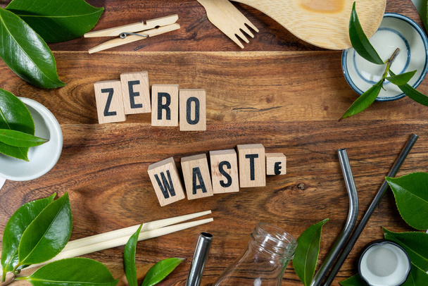 Der Holzklotz mit der Aufschrift "ZERO WASTE" auf Holzgrund. ECO-Konzept mit Recyclingsymbol und Blättern. - Foto, Bild