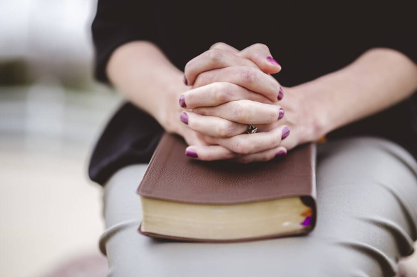 A woman  sitting with hand together on a book on her lap - Foto, Imagem