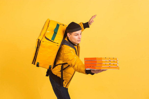 Contacless delivery service during quarantine. Man delivers food and shopping bags during insulation. Emotions of deliveryman isolated on yellow background. - Foto, Imagem