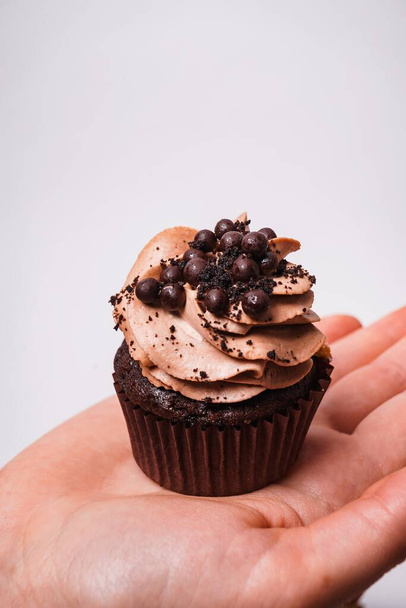 A vertical shot of a chocolate cupcake on man's hand on a white background - Foto, immagini