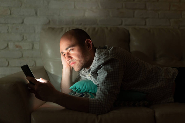 Attraente uomo calvo sms con il suo partner di notte mentre sdraiato su un divano a casa
 - Foto, immagini