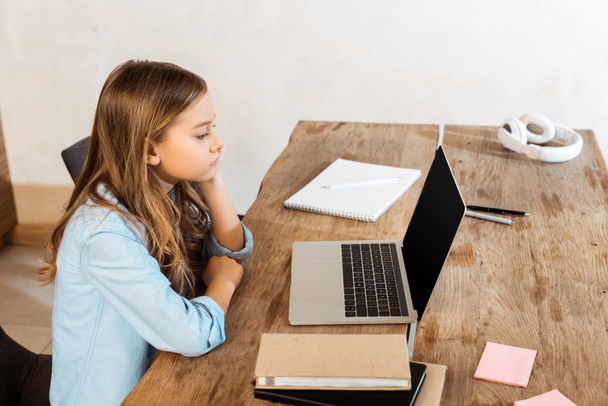 vista lateral del niño mirando a la computadora portátil con pantalla en blanco mientras estudia en línea en casa
  - Foto, imagen