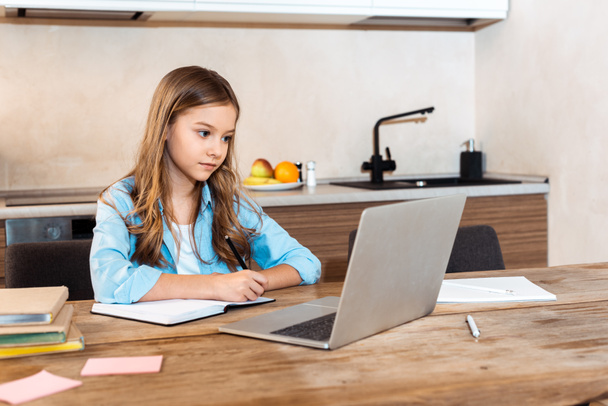 enfoque selectivo de niño lindo escribir en portátil cerca de la computadora portátil, mientras que el e-aprendizaje en casa
 - Foto, Imagen