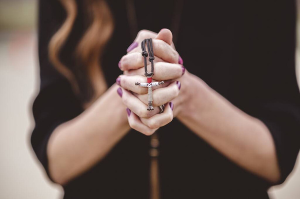 A shallow focus shot of a female wearing a black shirt while holding a cross in her hand - Foto, immagini