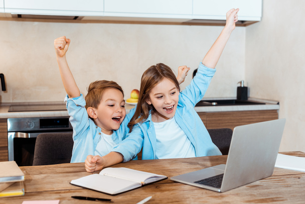 enfoque selectivo de los niños felices con las manos por encima de la cabeza mirando a la computadora portátil, mientras que el chat de vídeo en casa
 - Foto, Imagen