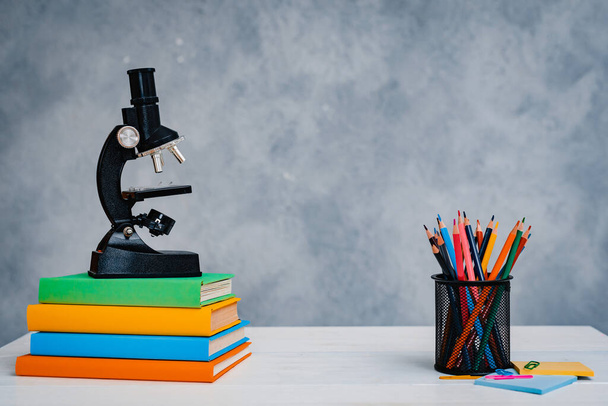 Una pila de libros de texto coloridos y un vaso de lápices brillantes sobre un fondo gris-azul
. - Foto, Imagen