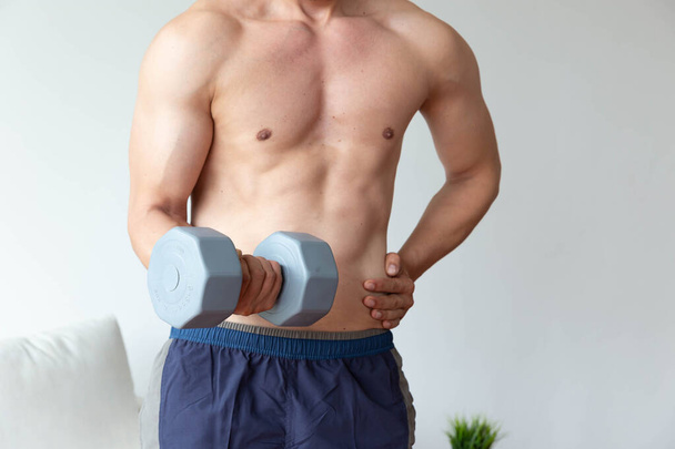 Athletic young man doing exercise with dumbbell in living room at home - Photo, Image