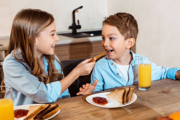 selective focus of happy sister feeding brother with toast bread at home - 写真・画像