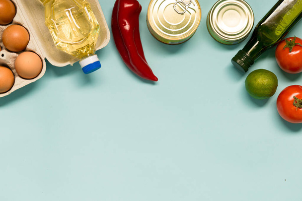Food product donations, oil bottle, chicken eggs and canned food top view isolated on blue background - Fotó, kép