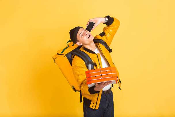 Contacless delivery service during quarantine. Man delivers food and shopping bags during insulation. Emotions of deliveryman isolated on yellow background. - Photo, image