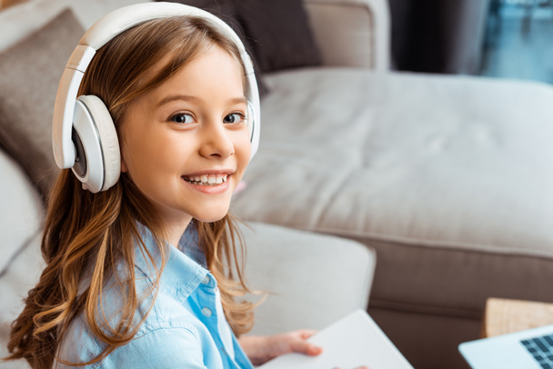 szczęśliwy dzieciak w słuchawkach bezprzewodowych patrząc w kamerę  - Zdjęcie, obraz