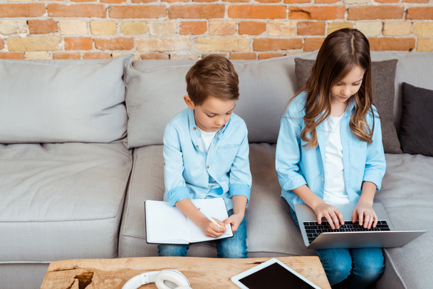 lindos hermanos en línea estudiando cerca de gadgets en casa
   - Foto, Imagen