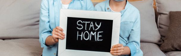 panoramiczne ujęcie rodzeństwa trzymającego tablicę z napisem w domu  - Zdjęcie, obraz
