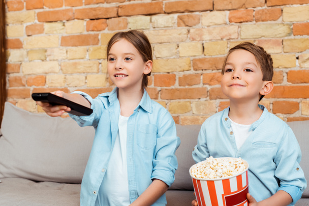 selectieve focus van kid holding afstandsbediening in de buurt van broer met popcorn emmer  - Foto, afbeelding