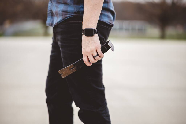 A shallow focus shot of a male holding an old wooden hammer while standing on the street - Photo, Image