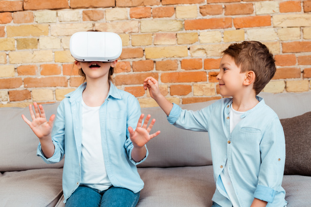 happy brother looking at surprised sister in virtual reality headset  - Foto, Bild