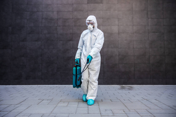 Full length of man in sterile uniform and mask sterilizing surface outdoors from corona virus, fungus and disease. - Foto, Imagen