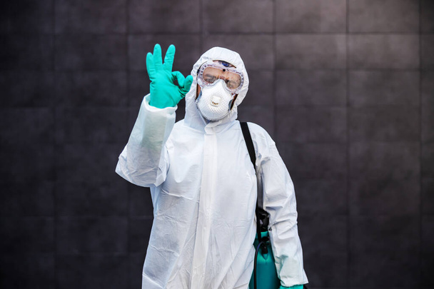 Portrait of man in sterile uniform and mask standing outdoors and showing okay sign. Surfaces are all sterilized from corona virus/ covid-19. - Photo, Image