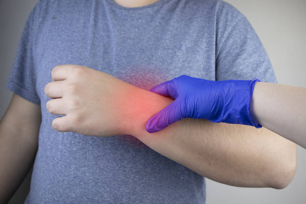 У чоловіка болить зап'ястя. Травматолог оглядає руку. Біль у зап'ястях як ознака тунельного синдрому або розтягнення, дегенерація сухожилля, артрит
 - Фото, зображення