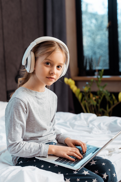 παιδί σε ασύρματα ακουστικά χρησιμοποιώντας φορητό υπολογιστή με e-learning στο υπνοδωμάτιο  - Φωτογραφία, εικόνα