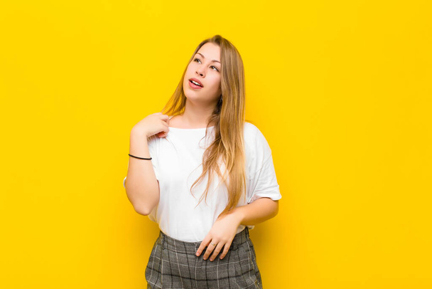 young blonde woman feeling stressed, anxious, tired and frustrated, pulling shirt neck, looking frustrated with problem against orange wall - 写真・画像