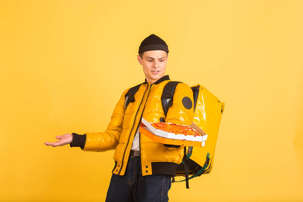 Contacless delivery service during quarantine. Man delivers food and shopping bags during insulation. Emotions of deliveryman isolated on yellow background. - Фото, зображення