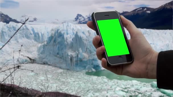 氷河の中でスマートフォンの緑の画面を使用して男性の手。緑の画面を必要な映像や画像に置き換えることができます。After Effectsやその他のビデオ編集ソフトウェアでキーエフェクトを使用することができます(YouTubeでチュートリアルを確認してください) 。).   - 映像、動画