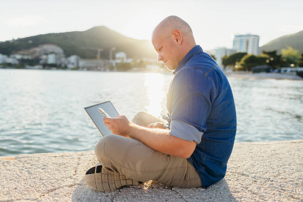 man travel and using laptop at seaside. Self employed man travel and consulting through internet. Holiday maker travel and using internet connection on beach. - Photo, Image