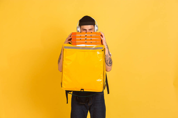 Contacless delivery service during quarantine. Man delivers food and shopping bags during insulation. Emotions of deliveryman isolated on yellow background. - 写真・画像