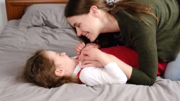 Happy little preschooler girl lying in comfy bed playing with smiling loving young mom at home, joyful mother tickling cute small daughter, laugh enjoy weekend in bedroom joking having fun together - Кадри, відео