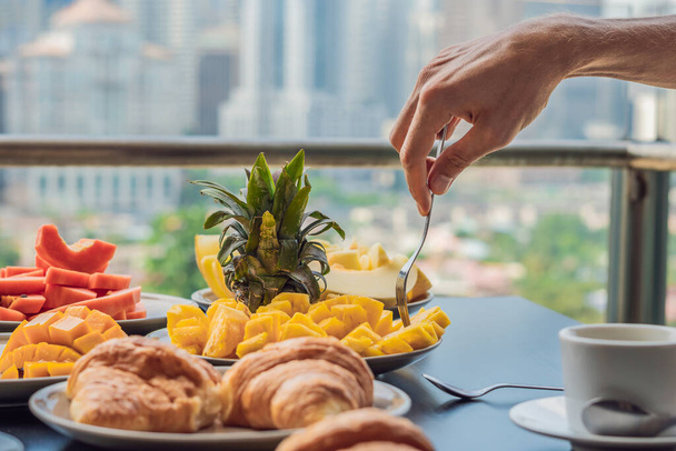 Coronavirus is over. Quarantine weakened. Take off the mask. Now you can go to public places. Breakfast table with coffee fruit and bread croisant on a balcony against the backdrop of the big city - Фото, зображення