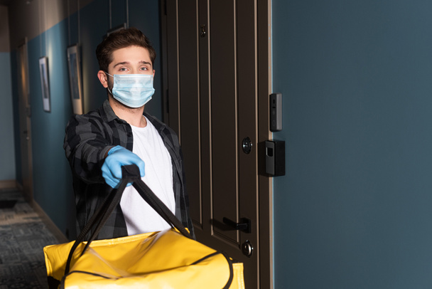 Delivery man in medical mask and latex glove holding thermo bag in entryway - Φωτογραφία, εικόνα