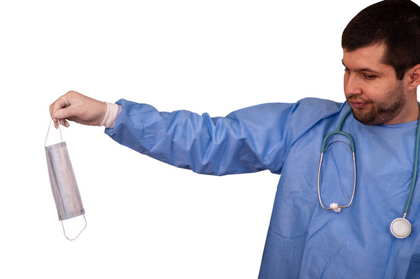 Lékař v lékařských šatech a stetoskopem, drží v ruce ochrannou masku infikovanou novým koronavirem nebo Covid-19, izolovat na bílém pozadí - Fotografie, Obrázek