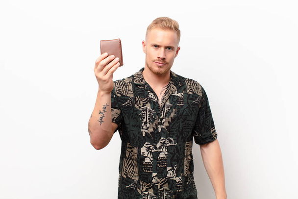 young blonde man making capice or money gesture, telling you to pay your debts! with a wallet - Foto, afbeelding