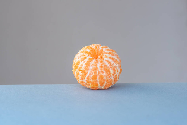 Oranssi mandariini ilman ihoa neutraalilla sinisellä ja harmaalla vaakasuoralla taustalla
. - Valokuva, kuva