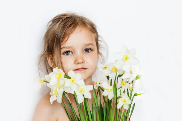 a little girl stands near a white wall, with a bouquet of daffodils, spring flowers, bouquet, beauty, gift to mother, daughter - 写真・画像
