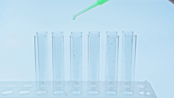przycięty widok naukowca dodającego zieloną szczepionkę do probówek z pipetą - Materiał filmowy, wideo