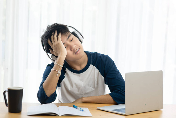 Asian teenager using headphone and laptop for online education, headache and seriously situation. - Foto, immagini