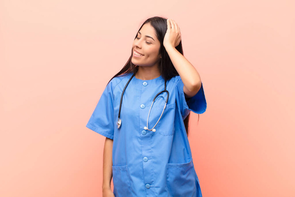 young latin nurse smiling cheerfully and casually, taking hand to head with a positive, happy and confident look against pink wall - Fotografie, Obrázek