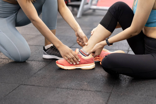 Asian young woman having ankle pain after workout at the gym. painful during exercise training and friends are here to help, encouragement - Foto, Bild