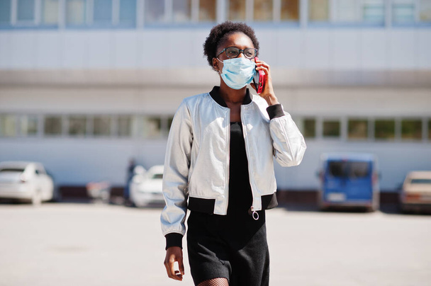 African woman wearing disposable medical mask and gloves walking outdoor and speaking phone during epidemic time. - Zdjęcie, obraz