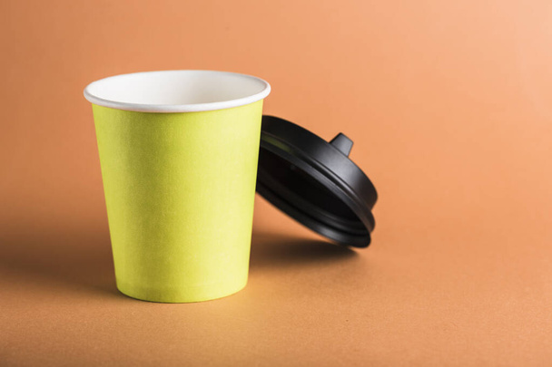 Egy zöld papír újrahasznosítható kávé kupa nyitott fekete fedővel, narancssárga háttérrel. Zéró hulladék koncepció közelkép másolási hellyel. Vízszintes tájolás. - Fotó, kép