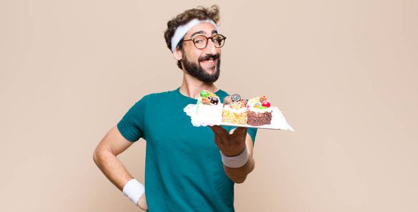 young sports man with cakes against flat wall - Foto, imagen