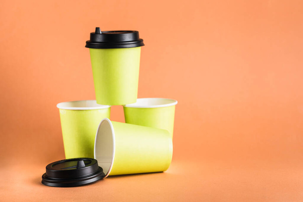 Een aantal groene papieren herbruikbare koffiekopjes met een gesloten zwart deksel op een oranje achtergrond. Zero waste concept close-up met kopieerruimte. Horizontale oriëntatie. - Foto, afbeelding
