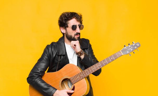 young musician man feeling ill with a sore throat and flu symptoms, coughing with mouth covered with a guitar, rock and roll concept - Photo, Image