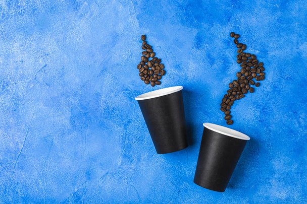 古典的な青の背景にコーヒー豆と2つの黒い紙再利用可能なコーヒーカップ。コピースペース付きのゼロ廃棄物コンセプトトップビュー。水平方向. - 写真・画像
