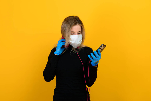 Retrato de una chica con una máscara médica, que se pone un guante de goma. Fondo amarillo y gris. Copiar espacio. - Foto, imagen
