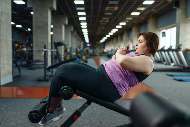 Overweight woman doing exercise on press with dumbbells in gym, active training. Obese female person struggles with excess weight, aerobic workout against obesity, sport club - Foto, Imagem