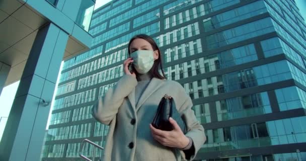 Woman in face mask talking on phone in business district - Séquence, vidéo