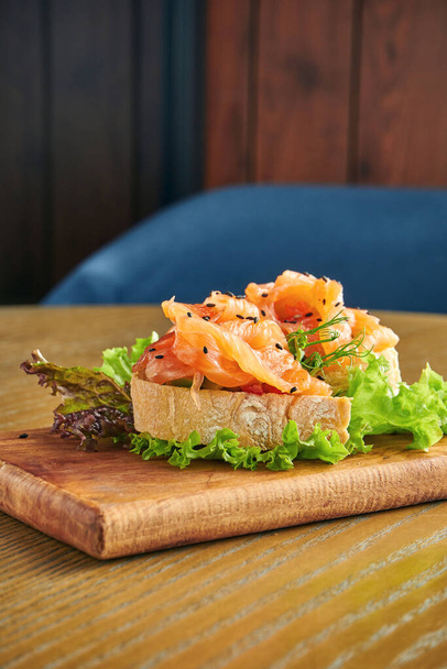 Appetizing bruschetta with salmon and lettuce on a cutting board on a wooden background. Close up, selective focus - Foto, Imagem